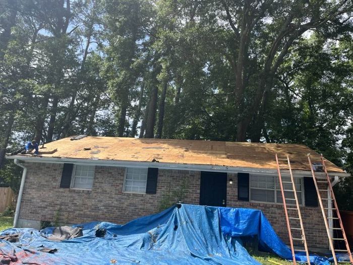 Old roof torn off a brick ranch, tarps protecting the yard